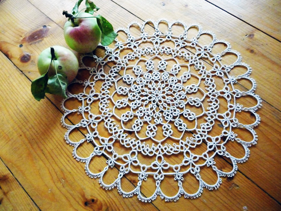 Beige tatting lace doily made with split rings and chains, lying on a wooden background next to a red apple. #FairyLacefromElena