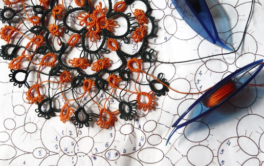 Bicolored tatting doily in progress with orange and dark green threads, two blue shuttles and printed pattern by FairyLacefromElena