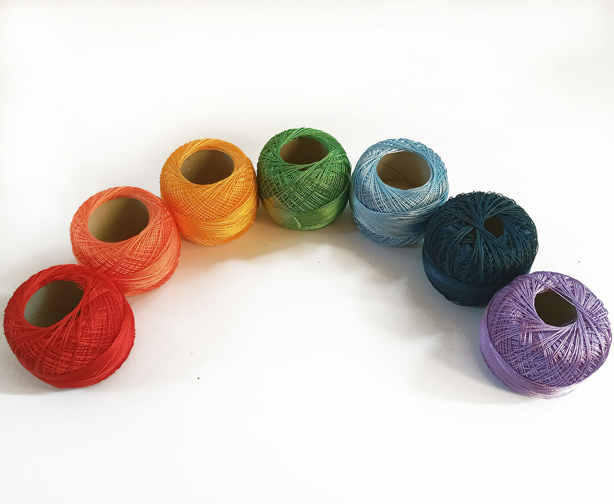 Seven colorful polyester thread balls for tatting lace, each 50g, placed in a rainbow semicircle, part of Tatting in resin tutorial series by FairyLacefromElena.