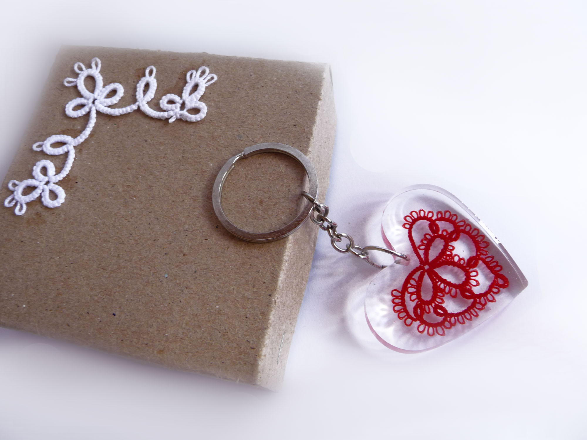 Red tatting lace heart keychain inside a transparent resin heart, placed in a gift box with white lace logo, handmade by FairyLacefromElena.